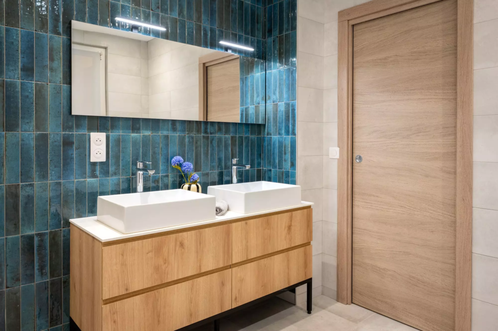 La salle de bain et son meuble double vasque, réhaussé d'une faïence effet zellige bleu